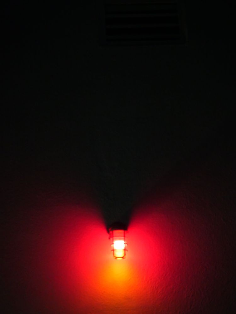 a caged red light mounted on a white wall at night (so there's nothing white about it)
