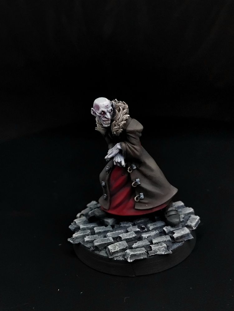 A bald vampire in a dark brown coat with a fur collar and red robe