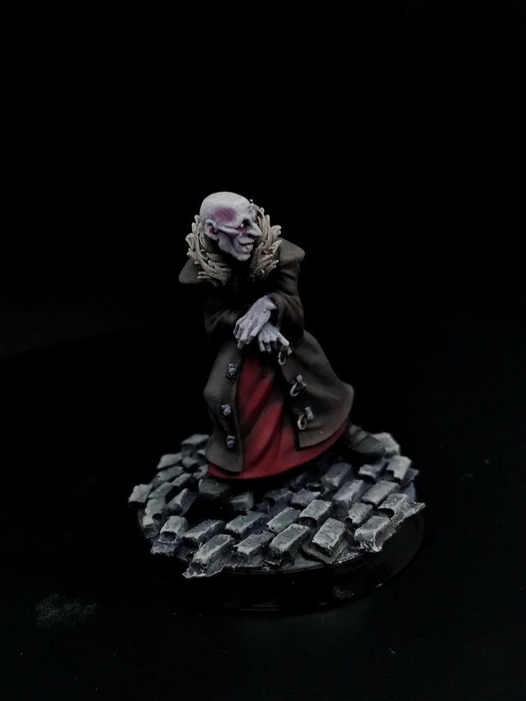 A bald vampire in a dark brown coat with a fur collar and red robe