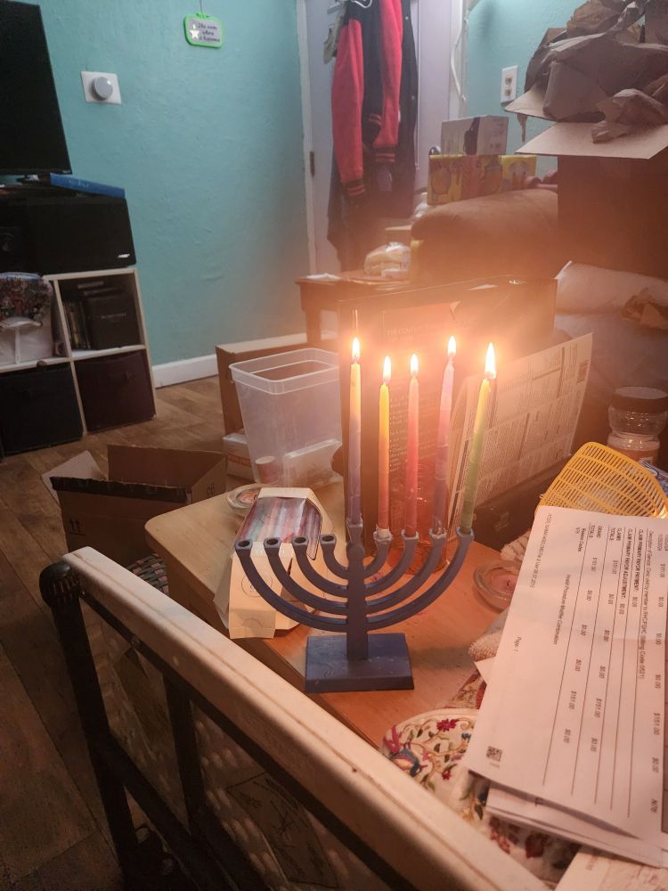 Blue hannukiah lit with multicolored candles for th fourth night of Chanukah, on a cluttered coffee table.