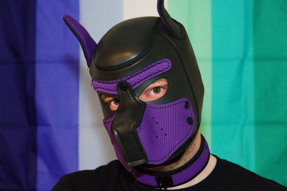 Finn in front of the man-love-man pride flag. The pride flag is blue, white and green striped. 