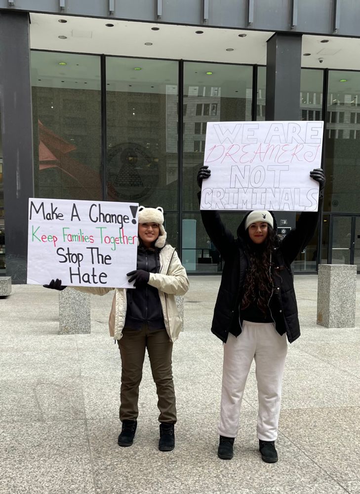 Two young women holding protest signs that say “Make a change! Keep families together, stop the hate” and “We are dreamers not criminals”