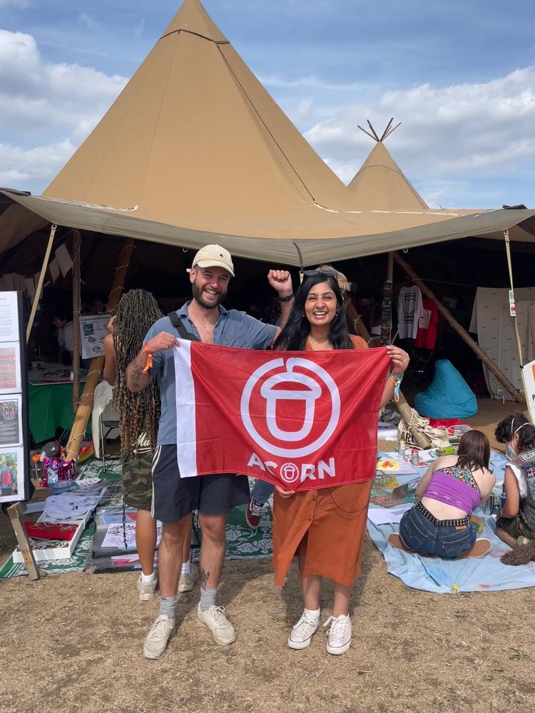 An ACORN member posing with a fist in the air, holding an ACORN flag with Zara Sultana outside a tent at the Forward Festival