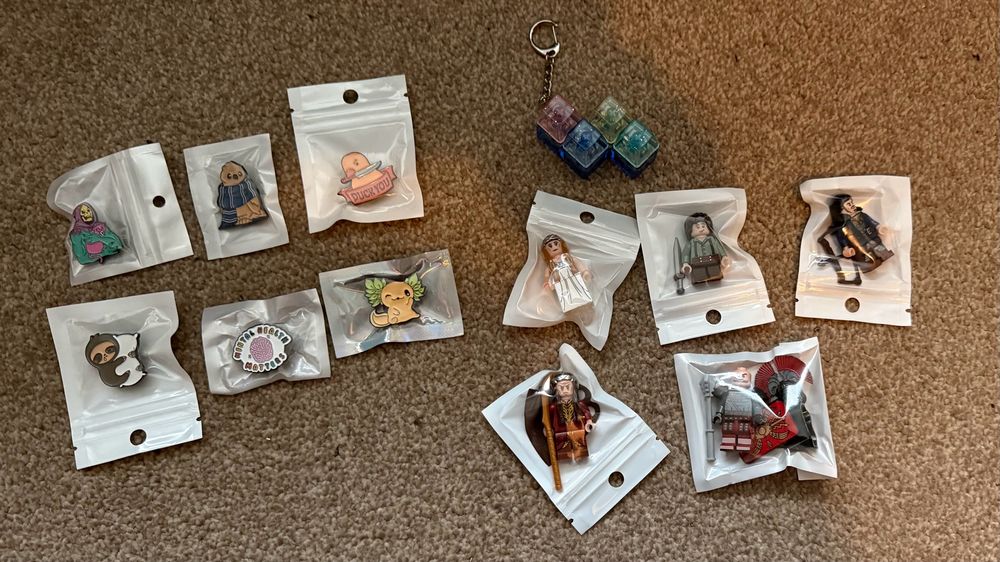 Various pin badges and Lord of the rings Lego minifigs, plus Roman minifig. Also a tactile button keyring.
