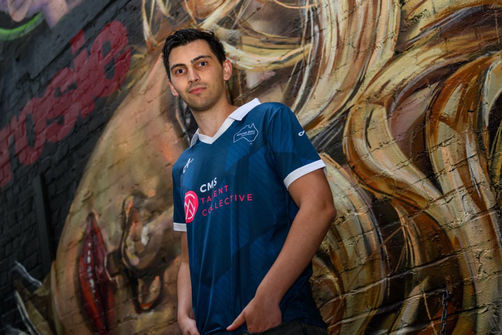 A man with black hair wearing a blue jersey with a white collar and trim standing in front of a wall with mural artwork