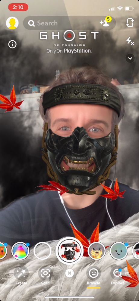 me trying out our snapchat filter right before the game launched. I have a fake mask and headband on with smoke in the background and pampas grass in the foreground and maple leaves blowing around me 