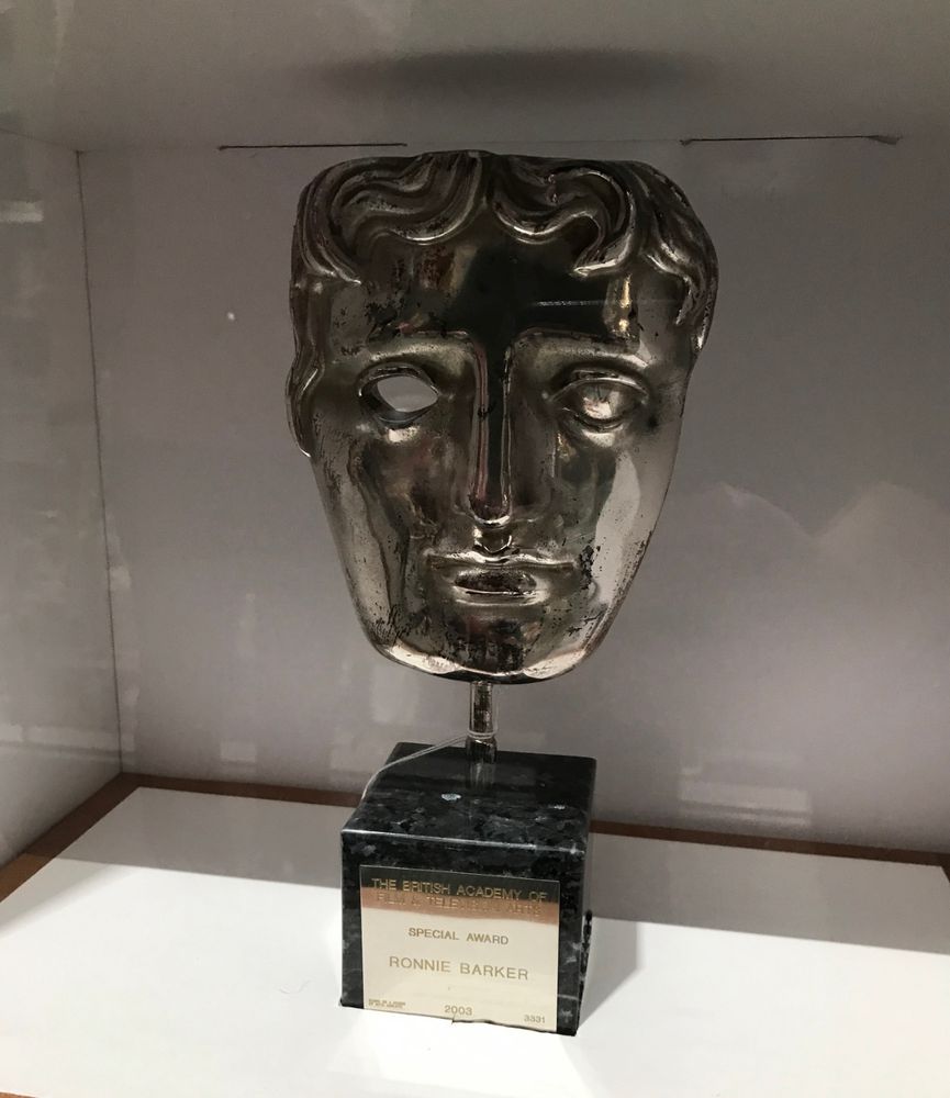 A BAFTA award that was presented to the great Ronnie Barker. A silver statue of a face on a little cube. The name of the recipient engraved on a plaque on the front. 