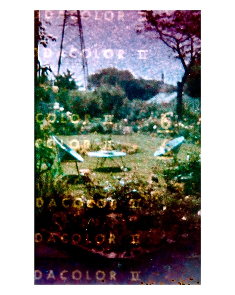 Very grainy film photo of a garden with space age furniture overlooked by a pylon, embossed with the words kodacolor II from the paper backing of the expired film roll circe 1970s 