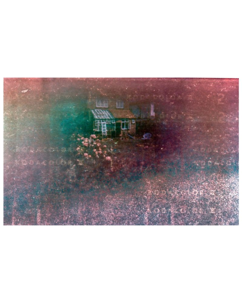 Very grainy film photo of a house and roses emerging from the film fog, embossed with the words kodacolor II from the paper backing of the expired film roll circe 1970s 