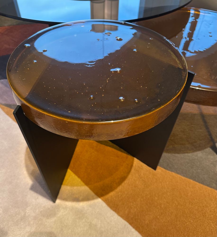 ett litet runt bord, med mycket tjock, lite bubblig, rund bordsskiva. färg på glaset är bränd karamell. på ett metallstativ i svart v.