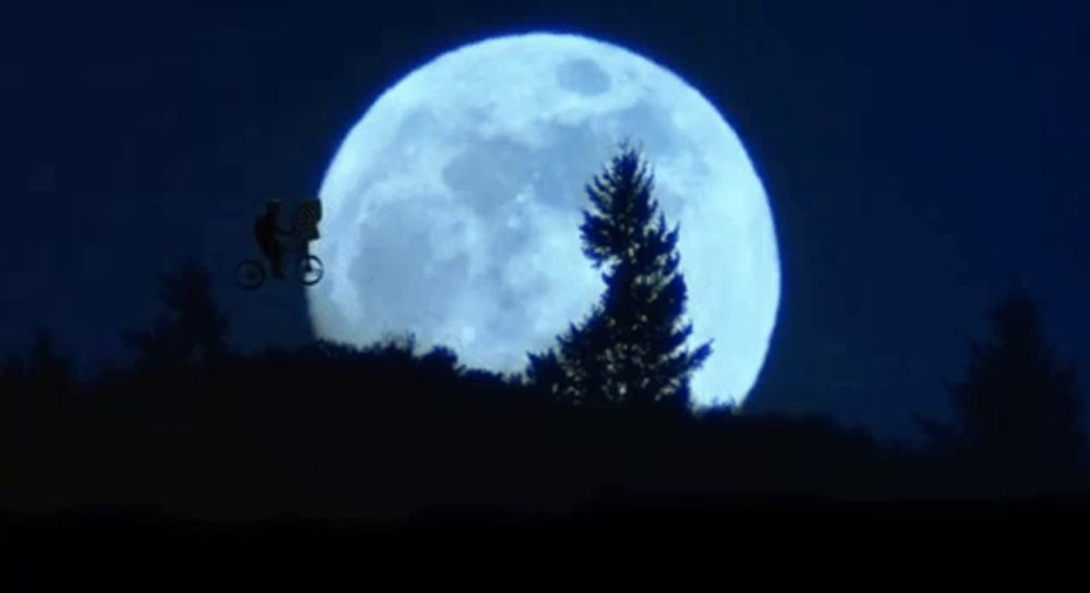 a man on a bike is flying in front of a full moon