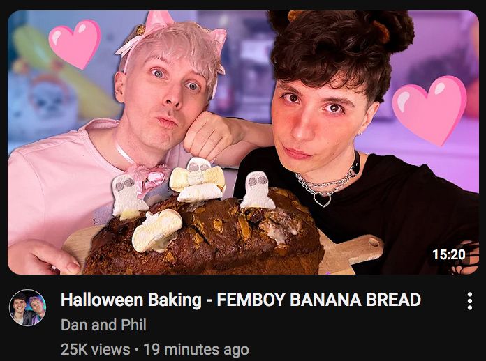 dan and phil youtube thumbnail: Halloween Baking - Femboy Banana Bread

Phill is in a pink cat costume and dan is in a black bear costume. there is a picture of a banana bread loaf in front of them with ghost decorations on top