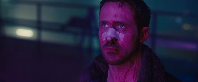 Ryan Gosling as "K" from Blade Runner 2049. His face is bruised in many places, and he looks up despondent while bathed in a pink light