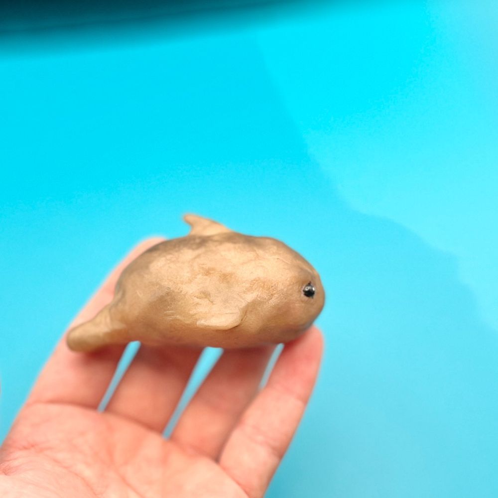 Against a solid background, a hand holds a small sculpture of a potato whale hybrid