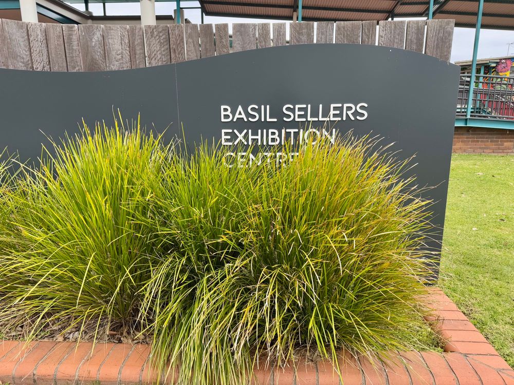 Signage at the Basil Sellers Exhibition Centre in Moruya, partially obscured by lomandra.