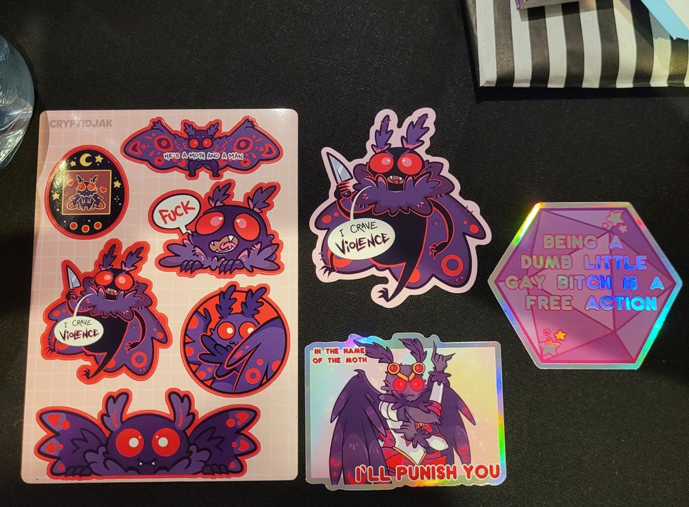 A sticker sheet of mothman stickers, an individual sticker of mothman carrying a knife and saying "I crave violence, another of mothman saying "In the name of the moth I'll punish you, and a pink hologram sticker in the shape of a d20 saying "Being a Dumb Little Gay Bitch is a Free Action".