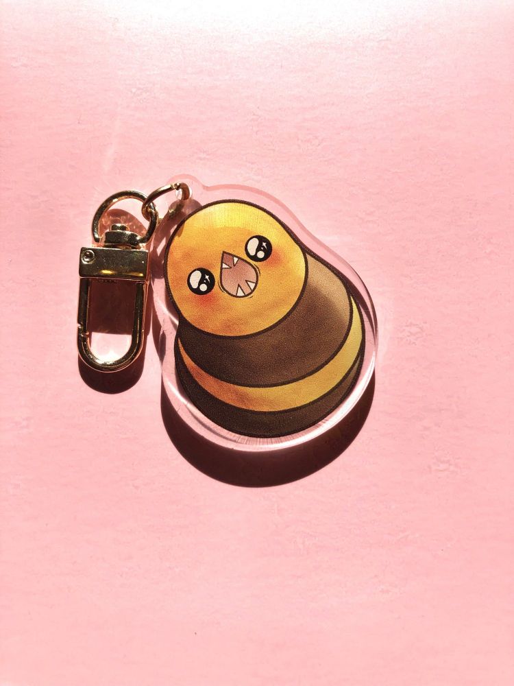 A photo of an acrylic keychain featuring an illustration of the great serpent of ronka from FFXIV, with very sparkly cute eyes and blushy cheeks.