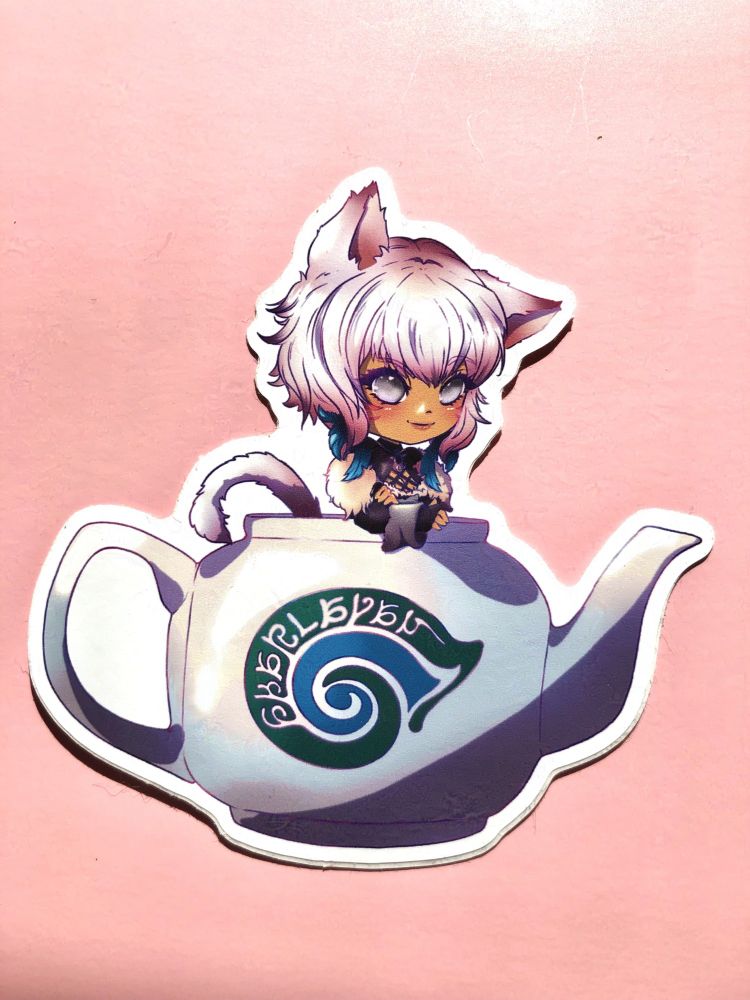 A photo of an acrylic keychain charm featuring an illustration of a chibi style Y'shtola in her Endwalker gear, sitting in a Sharlayan "The Last Stand" teapot.