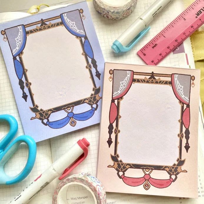 A photograph of a pair of memo pads based on some metallic, fabric-adorned frames inspired FFXIV. There are two colorways, one red, and one blue.