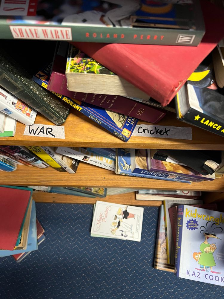 A bookshelf with two labels: ‘war’ and ‘cricket’