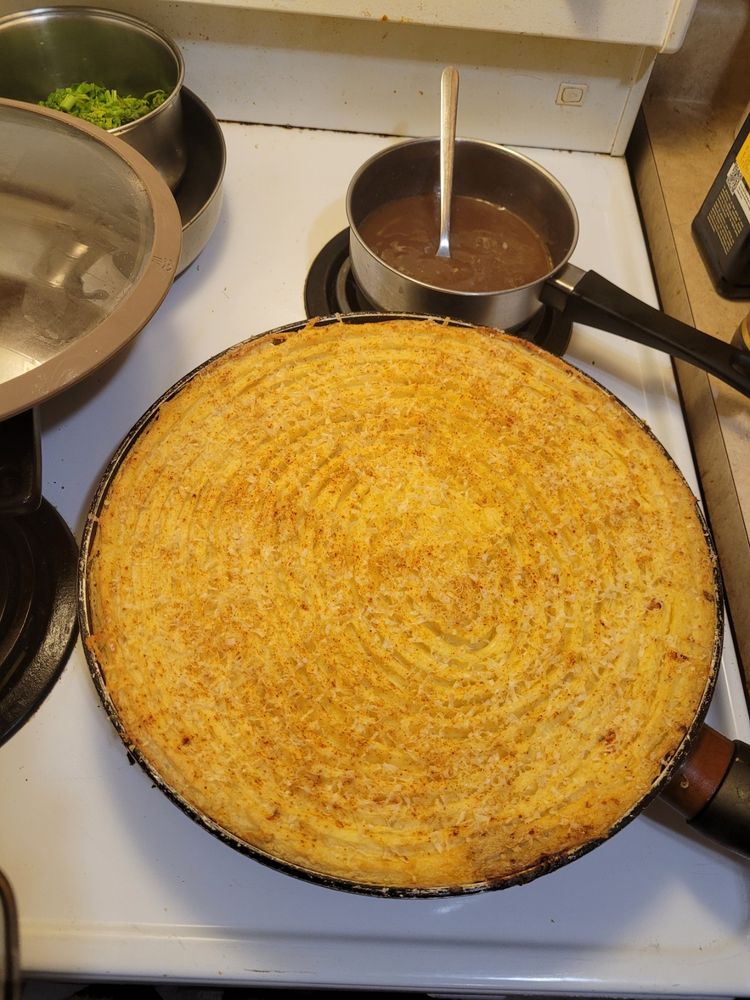 a stovetop with broccoli, gravy, and in the foreground, a large round pan in which can be seen the raked, browned mashed potato topping of this (birthday request) Shepherd's Pie, courtesy of Keisha.