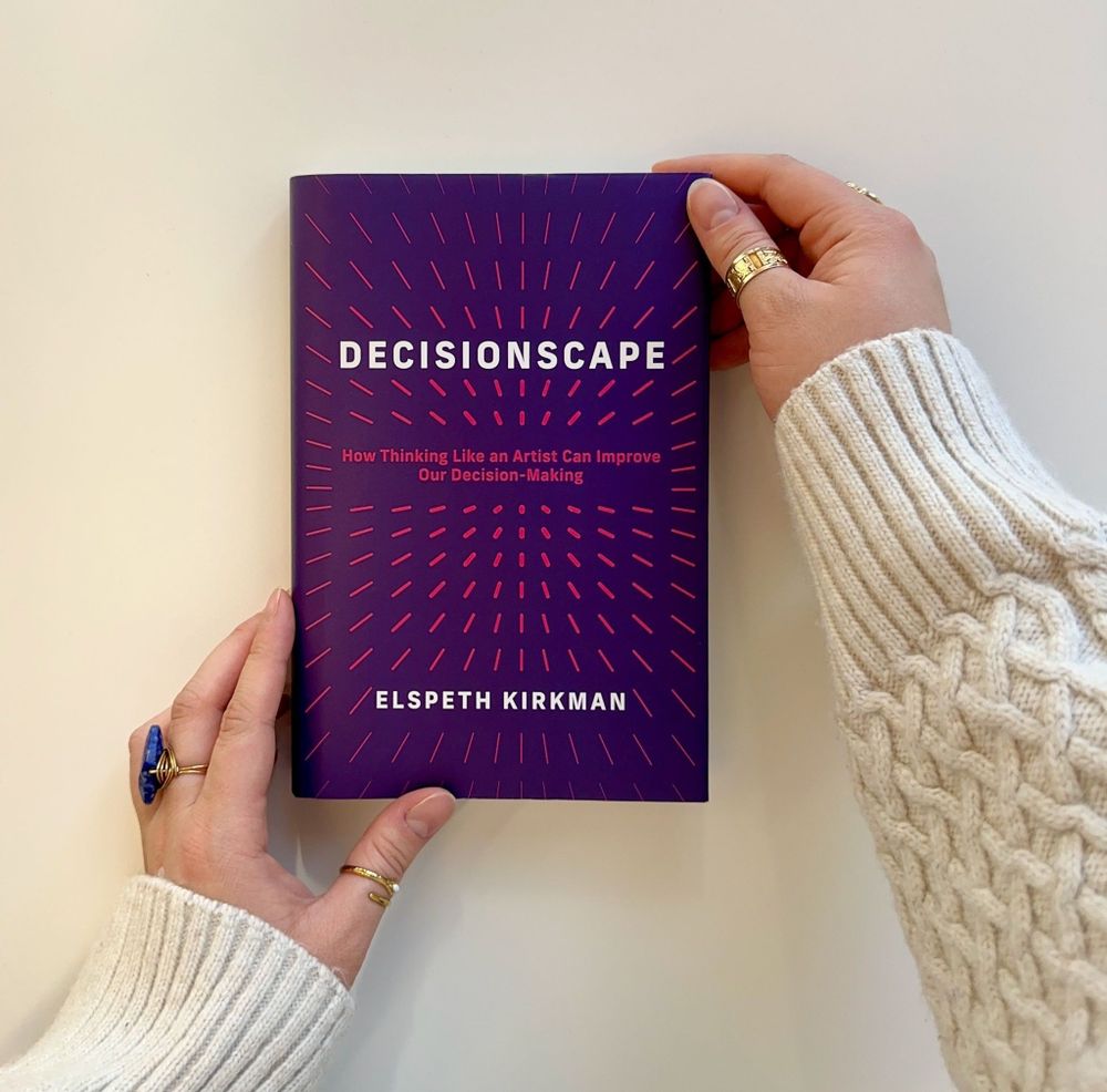 hands holding a copy of "Decisionscape: How Thinking Like an Artist Can Improve our Decision-Making" on a white background.