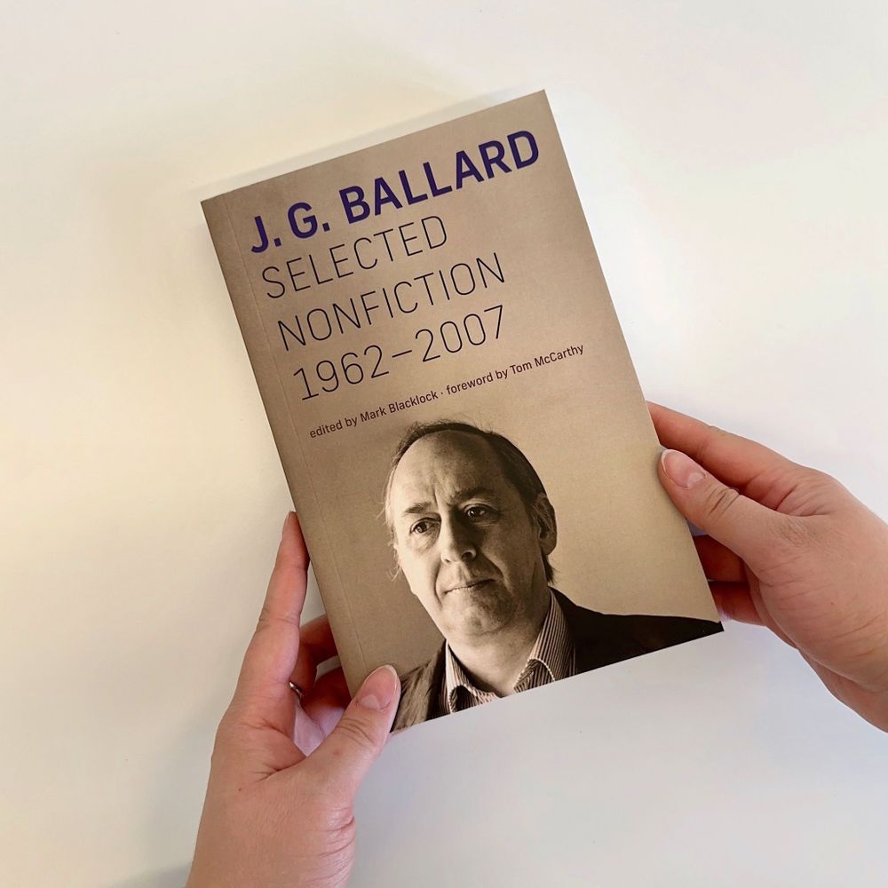 Hands holding a copy of "Selected Nonfiction, 1962–2007" by J. G. Ballard, edited by Mark Blacklock. The cover features a sepia-toned photo portrait of Ballard.