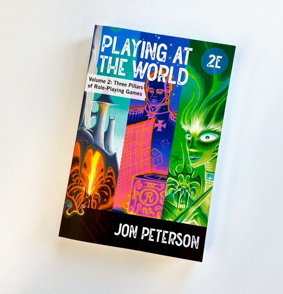 "Playing at the World, 2E" on a white background. Copy below the title reads "Volume 2: Three Pillars of Role-Playing Games." The cover features vivid illustrations of medieval and fantasy characters.