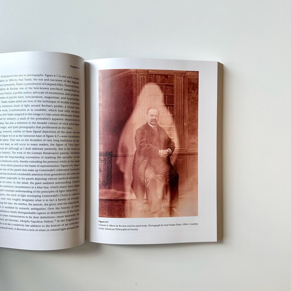 Open page from "Picturing Aura." Text is visible on the left, the right page is a sepia-toned photograph of a seated man. The outline of another figure overlaps his portrait.