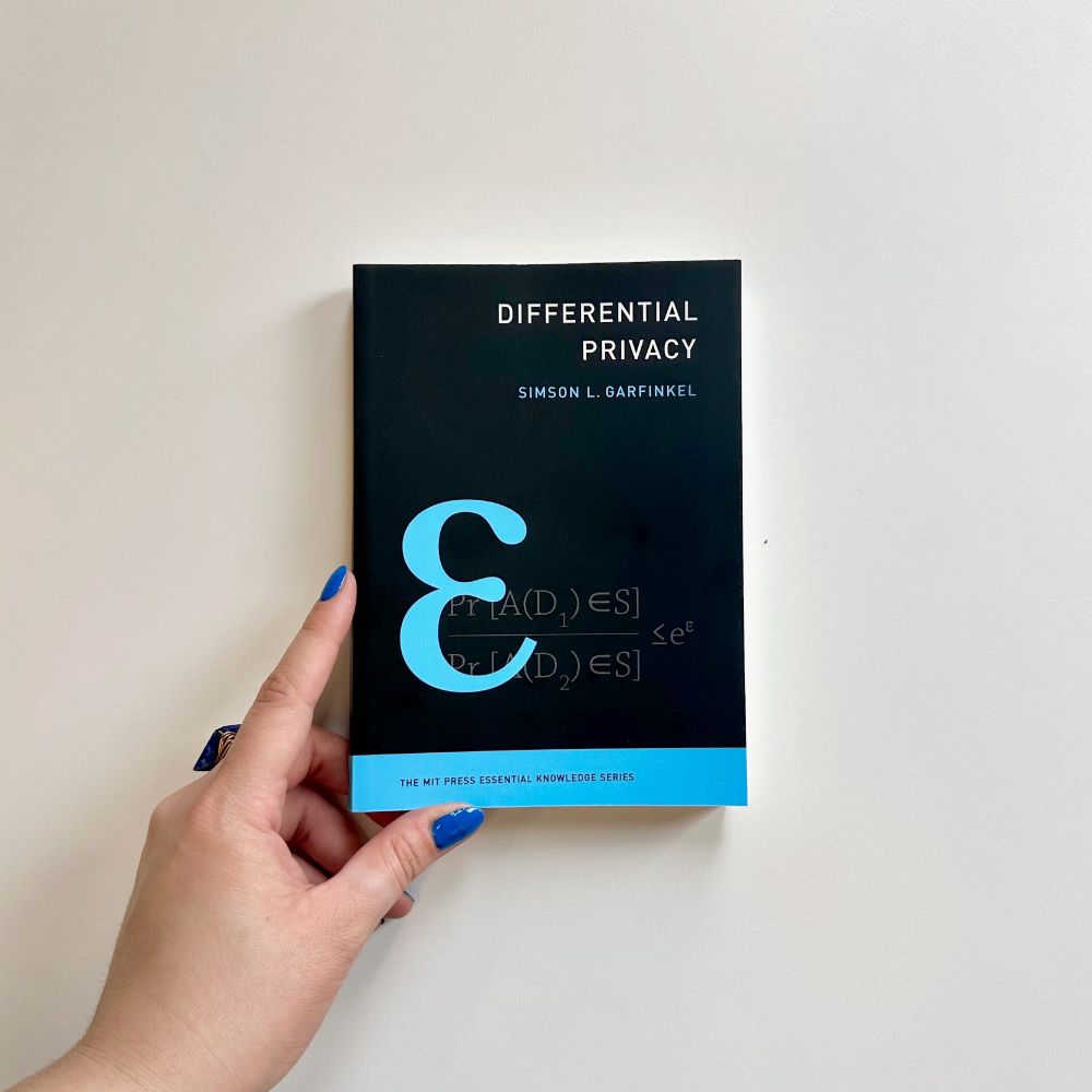 A hand holding a copy of "Differential Privacy." The features an illustration of an equation.