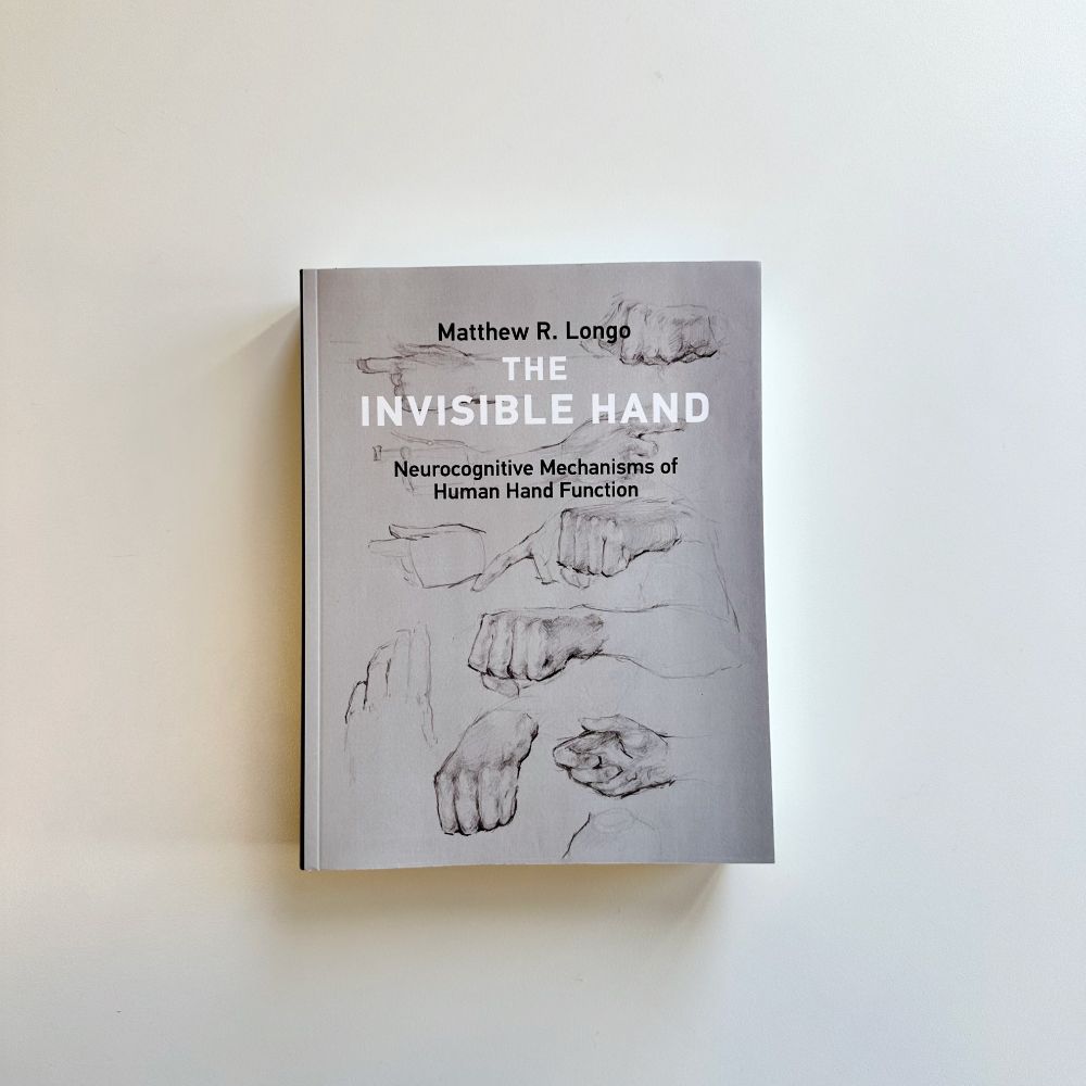 "The Invisible Hand: Neurocognitive Mechanisms of Human Hand Function" on a white background. The cover is grey and features various sketches of hands.