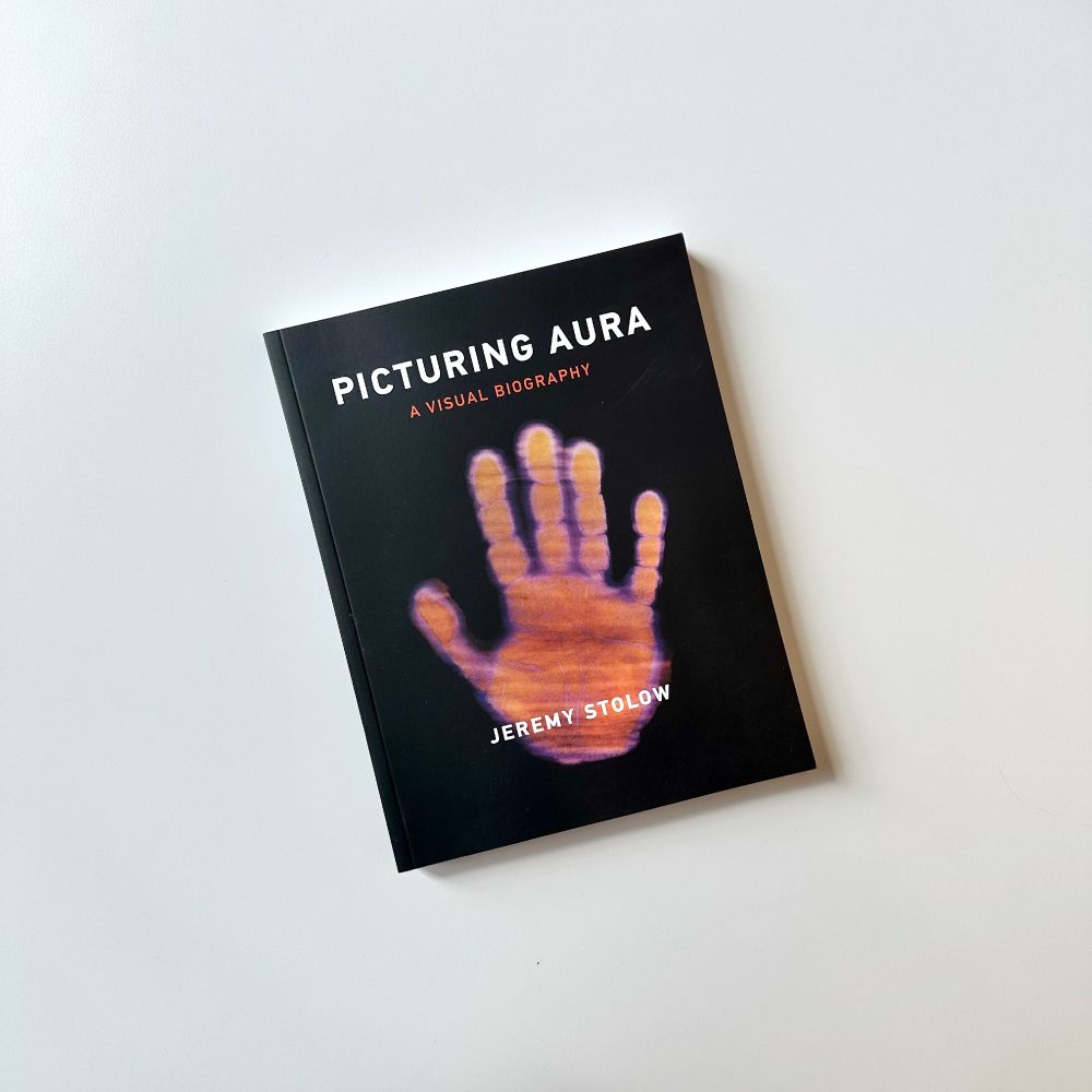 "Picturing Aura: A Visual Biography" on a white background. The cover is black with an image of red handprint.