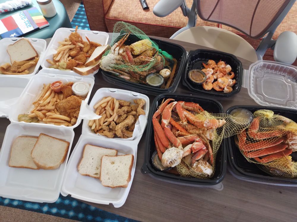 A spread of various containers full of crab legs, shrimp, fried catfish, bread and chicken.