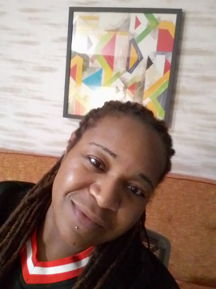 Black dyke with long brown locs & a labret smirking in a selfie.