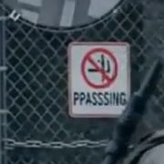 A screenshot from a ai generated video game video (it’s complete slop). It’s a sign on a fence that has some weird nonsensical figure in a red slashed out circle. Underneath it is the word PPASSSING