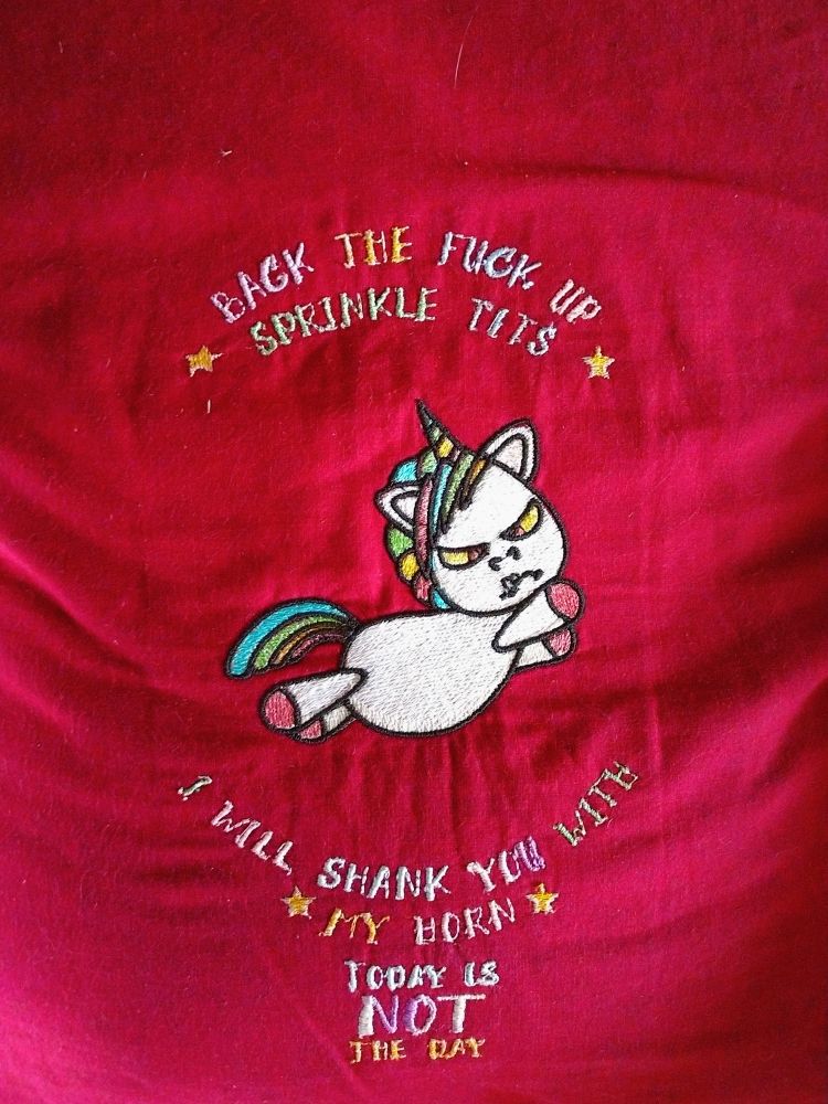 A pillow with an angry embroidered unicorn in mid-leap.  The text reads, "Back the fuck up sprinkle tits. I will shank you with my horn. Today is NOT the day."