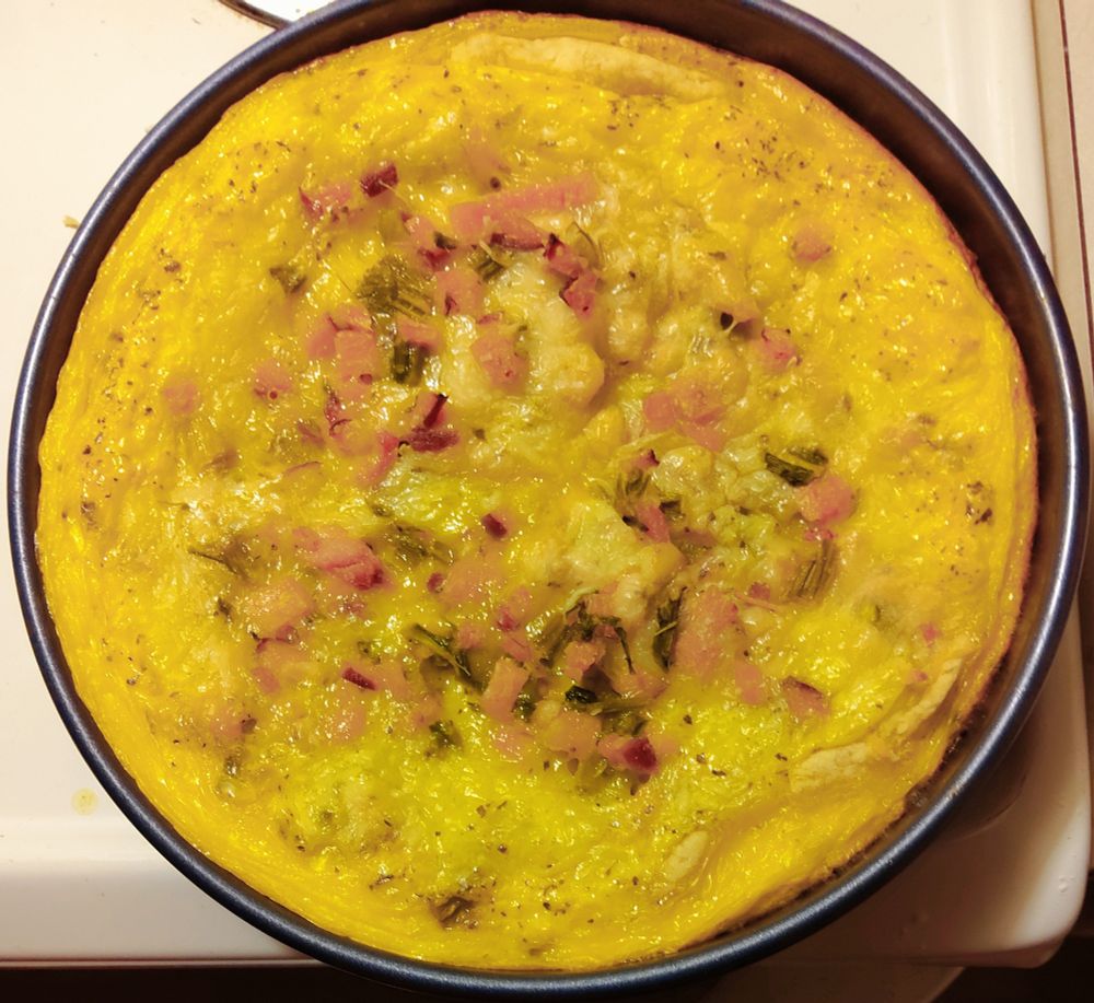 Homemade ham-and-asparagus quiche, still in its pan, on a white stovetop.