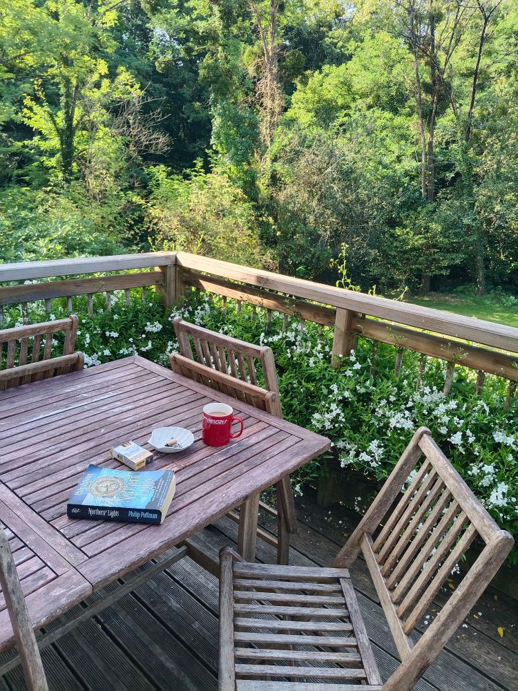 Ein Balkon mitten im Grünen, an einem Tisch liegen ein Buch und Zigaretten, außerdem ein kaffee