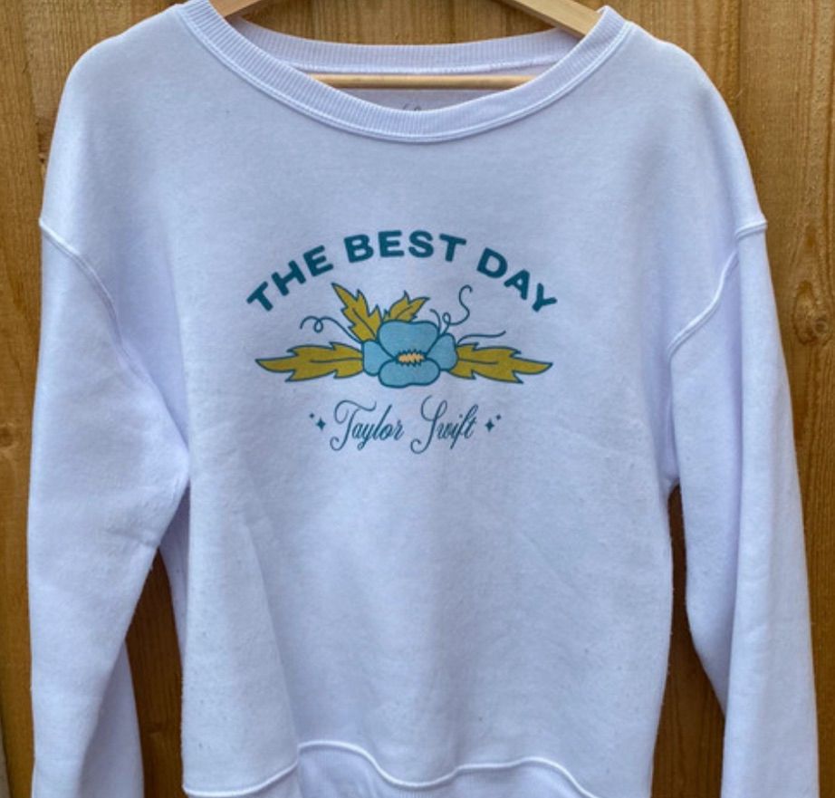White crewneck with “The best day “ in blue text and an image below of a floral pattern blue and yellow. Below with Taylor swift cursive centred text