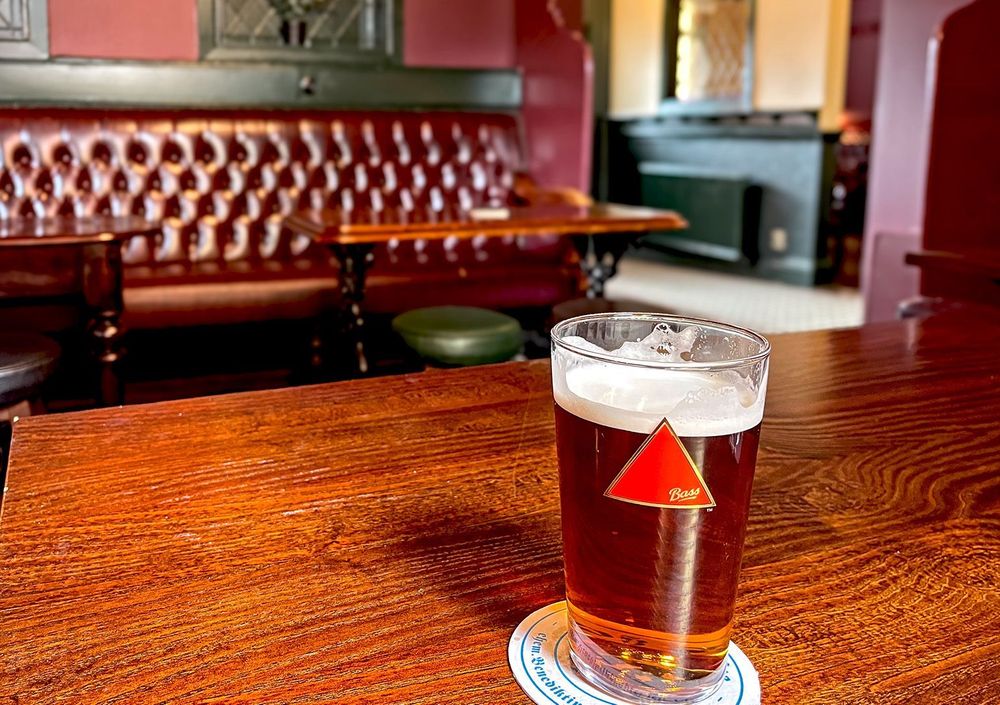 Close up of a pint of Draught Bass with the main room and lobby in the background.