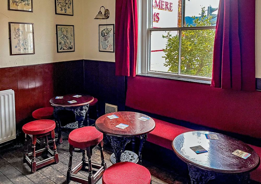 Side room with red upholstered bench and stools and wood panelled lower walls with framed cartoons above.