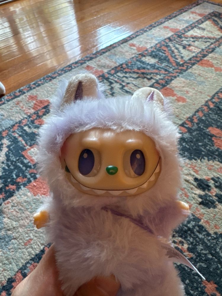 A furry light-purple doll with a big pointy-toothed smile. It has bunny ears and its purple eyes are unfocused, the left eye looking to the far left of the face and the right eye looking to the far right. 