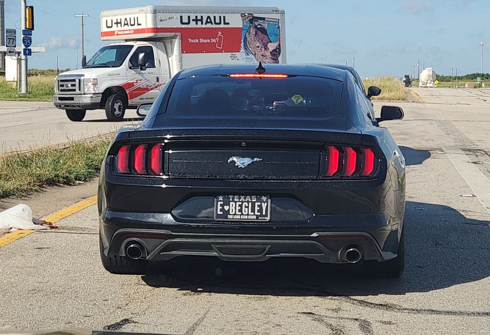 A black mustang with a black Texas personalized license plate reading E Begley.