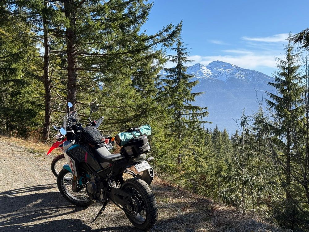 Photo of an Ibex 450 and CRF250L from the rear on a dirt road. Behind them is a gap in the trees with the snowy top of Mt Pilchuck peaking through. 