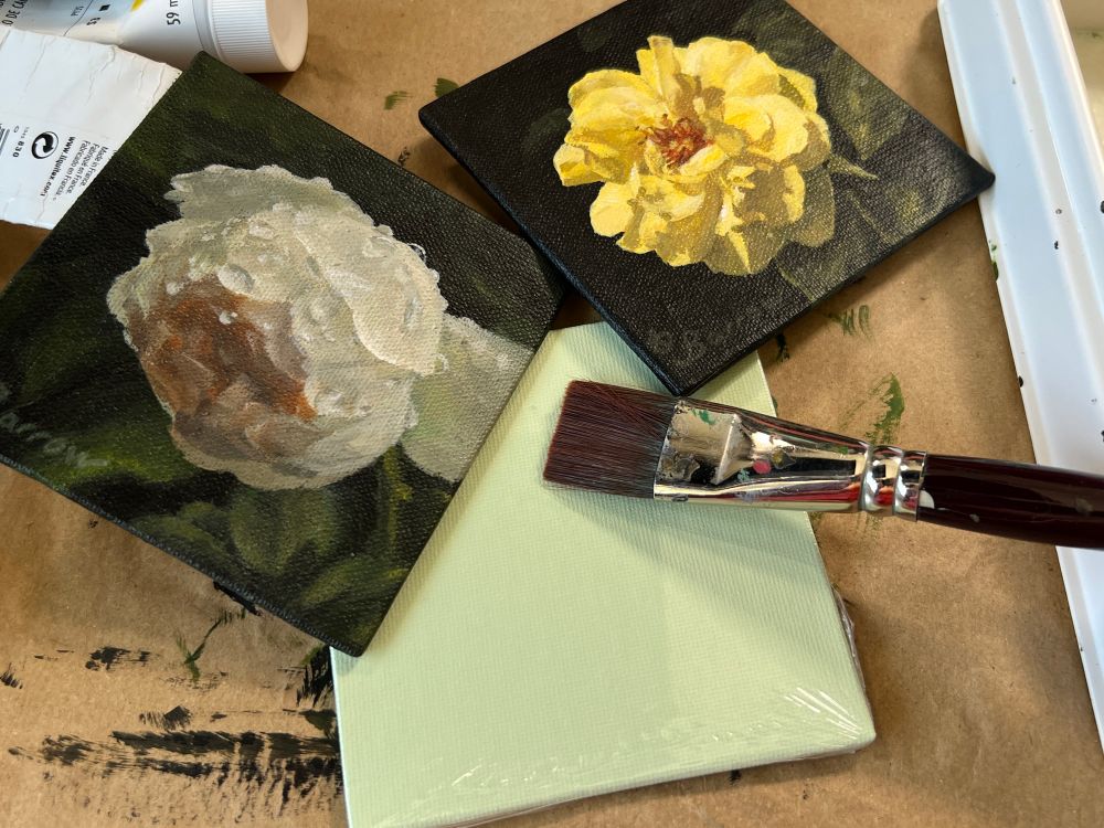 Photo of three mini canvases. Two are painted with flowers as the subject. One is blank and a paintbrush rests on it.