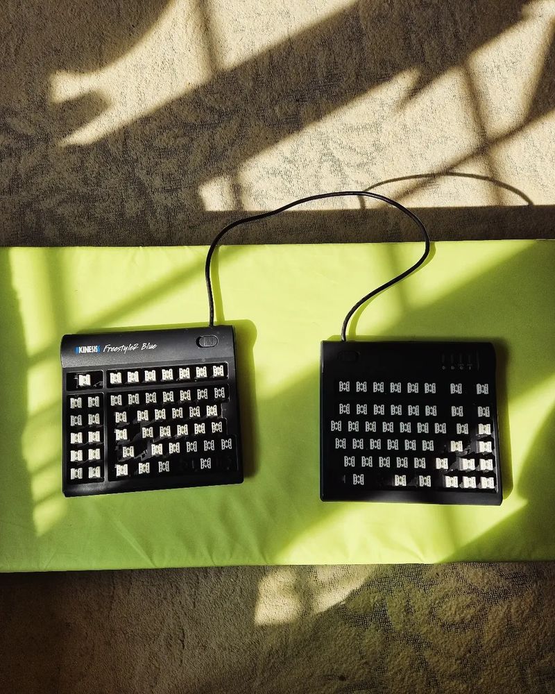 Green mat, shadows, and an ergonomic split keyboard with the keys taken off.