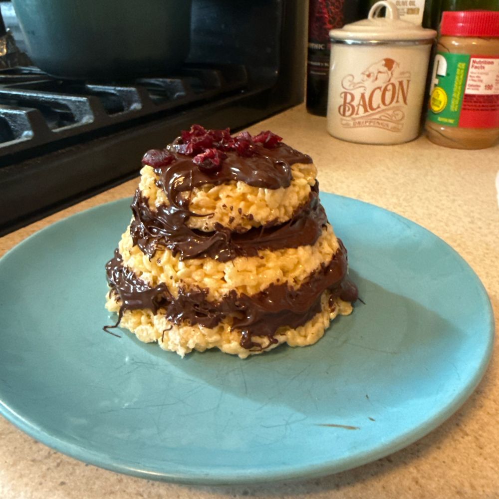 Mini Rice Krispie layer cake with chocolate frosting and craisins that looks like it was made by a toddler. 