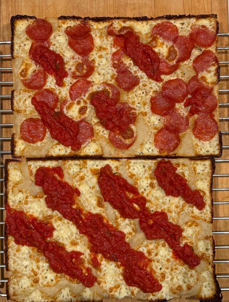 Two Detroit style pizzas, one pepperoni one cheese with a few racing stripes of tomato sauce on each. 