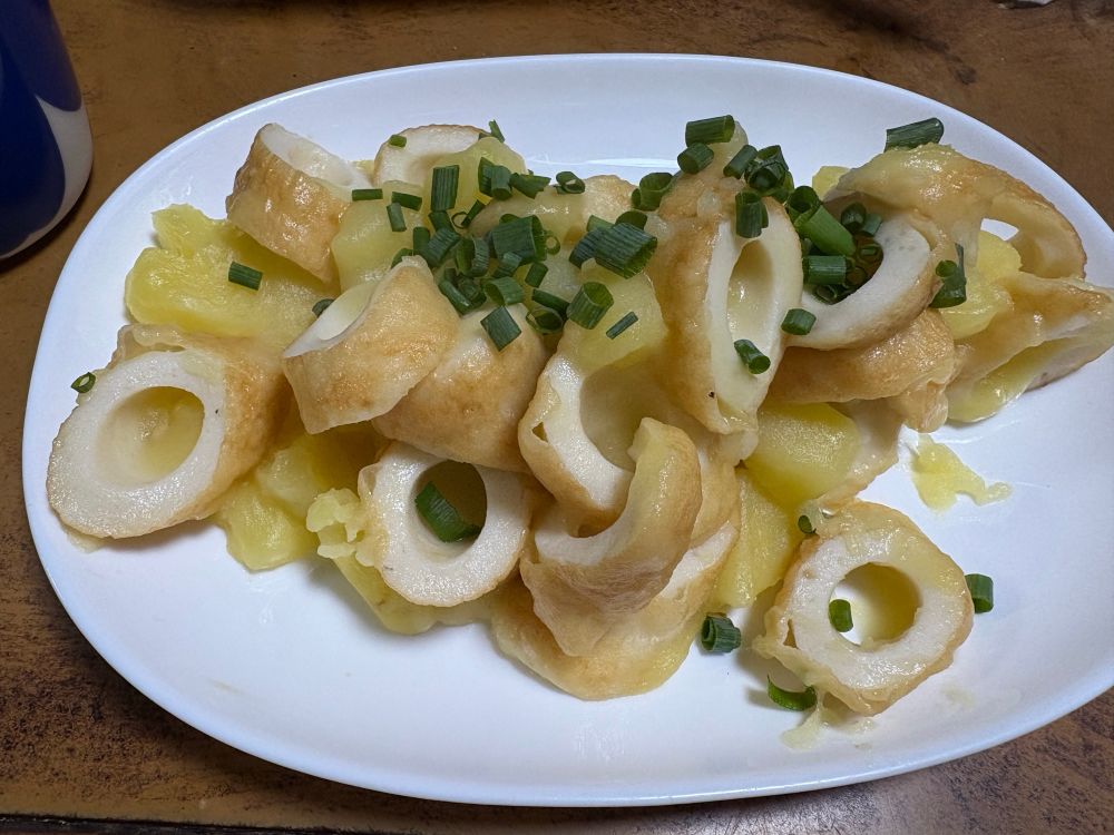 白い楕円形の皿に、ちくわとじゃがいものバター煮(小ネギを散らしたもの)を盛っている。