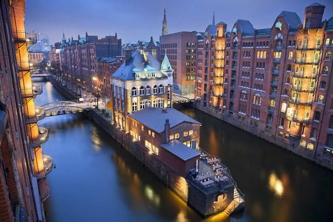A view of Hamburg, Germany in the evening with buildings lit up along a river with a bridge